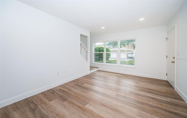 unfurnished room with light wood finished floors, stairway, and baseboards