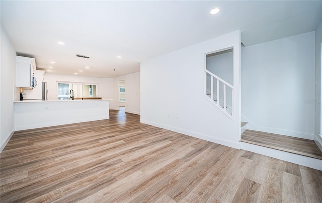 unfurnished living room featuring recessed lighting, visible vents, stairway, a sink, and light wood-type flooring