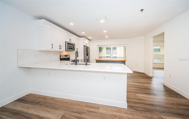 kitchen featuring wood-type flooring, kitchen peninsula, appliances with stainless steel finishes, and white cabinets