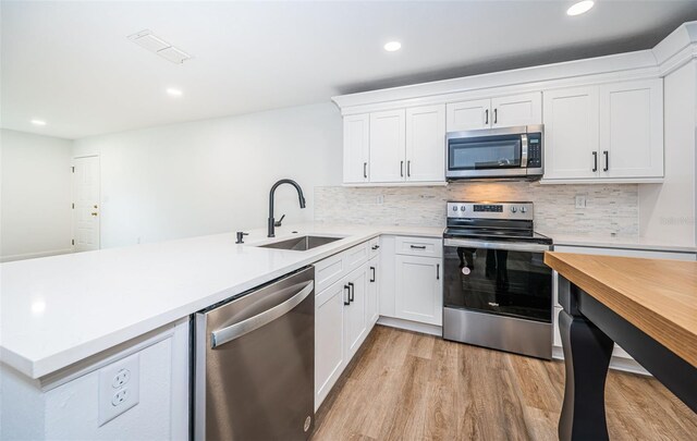 kitchen featuring light wood finished floors, stainless steel appliances, light countertops, white cabinetry, and a sink