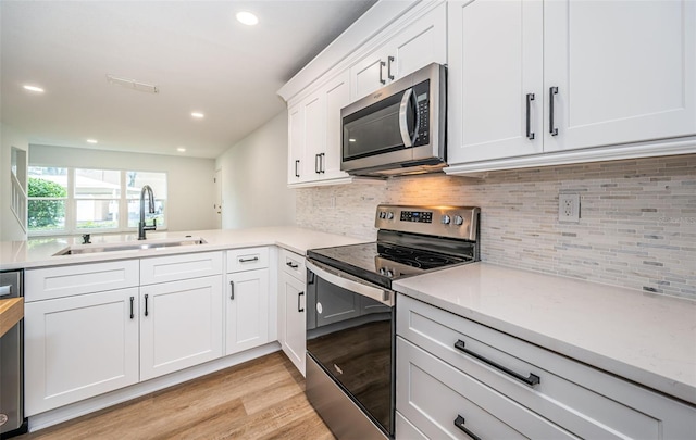 kitchen featuring appliances with stainless steel finishes, light wood-type flooring, white cabinetry, a sink, and recessed lighting