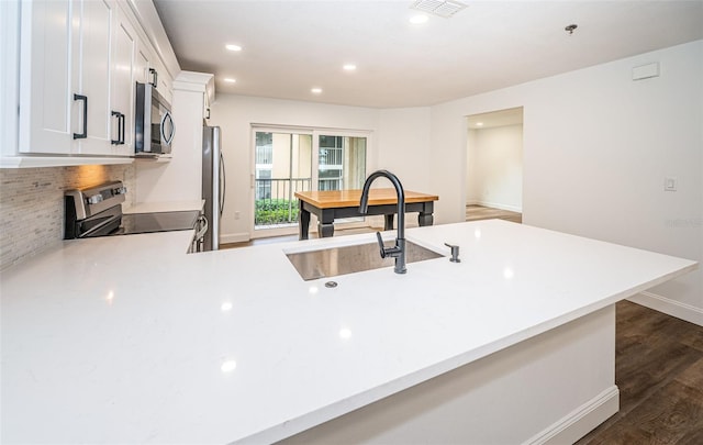 kitchen featuring appliances with stainless steel finishes, dark wood-type flooring, a peninsula, light countertops, and a sink