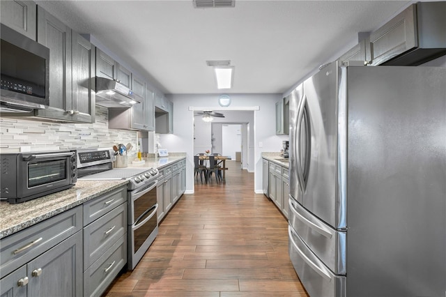 kitchen featuring light stone countertops, decorative backsplash, dark hardwood / wood-style flooring, appliances with stainless steel finishes, and gray cabinets