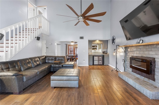 living room featuring a brick fireplace, ceiling fan, hardwood / wood-style floors, and a high ceiling