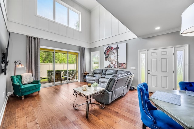 living room with hardwood / wood-style floors, a wealth of natural light, crown molding, and a towering ceiling