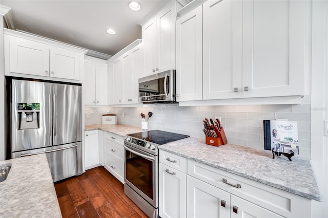 kitchen with light stone countertops, dark hardwood / wood-style flooring, appliances with stainless steel finishes, decorative backsplash, and white cabinetry