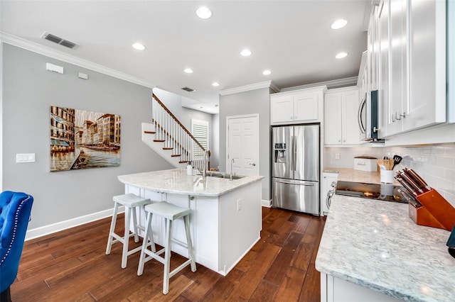 kitchen with appliances with stainless steel finishes, white cabinetry, sink, dark hardwood / wood-style floors, and a center island with sink