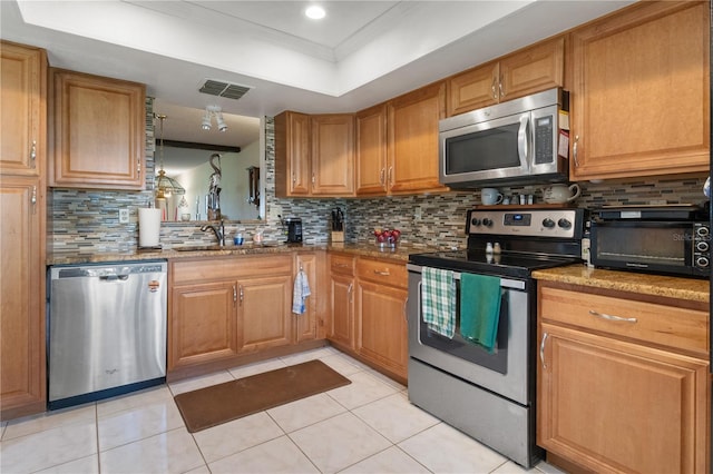 kitchen featuring appliances with stainless steel finishes, a tray ceiling, brown cabinets, and backsplash