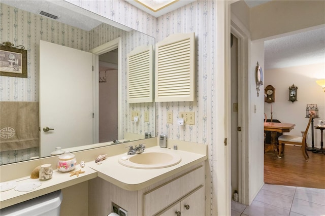 bathroom with a textured ceiling, tile patterned flooring, vanity, visible vents, and wallpapered walls