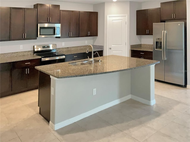 kitchen featuring stone countertops, light tile patterned floors, an island with sink, stainless steel appliances, and sink