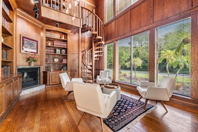 living area featuring wood walls, built in features, wood-type flooring, a high ceiling, and a fireplace