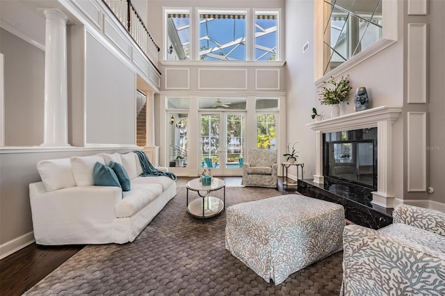 living room with hardwood / wood-style floors, a premium fireplace, a high ceiling, crown molding, and ornate columns