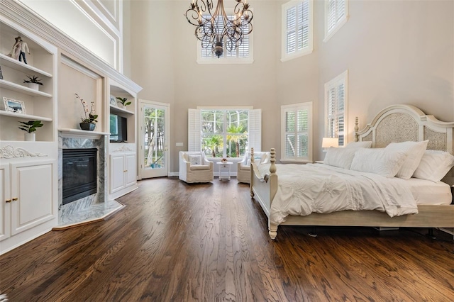 bedroom with an inviting chandelier, access to exterior, a premium fireplace, dark hardwood / wood-style flooring, and a towering ceiling