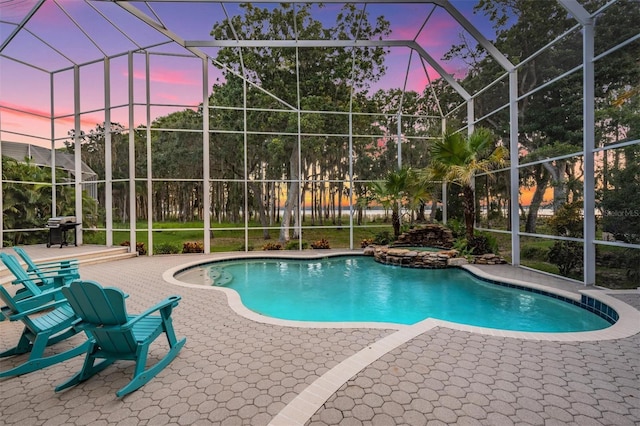 pool at dusk with an in ground hot tub, glass enclosure, and a patio