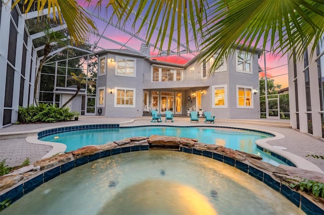 pool at dusk featuring a lanai, an in ground hot tub, and a patio area