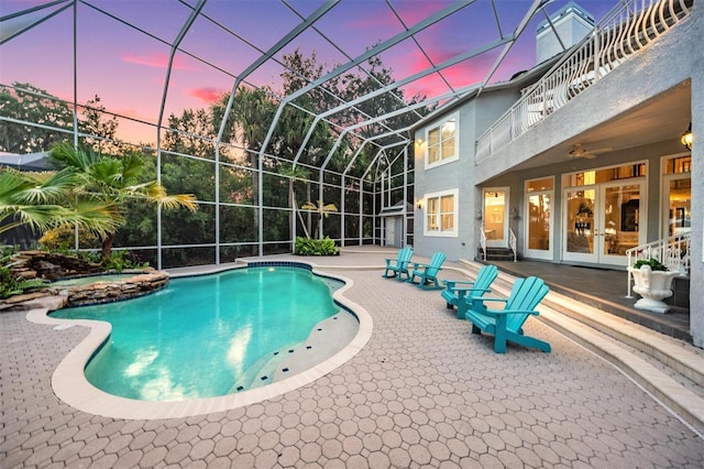 pool at dusk featuring ceiling fan, french doors, a lanai, and a patio area