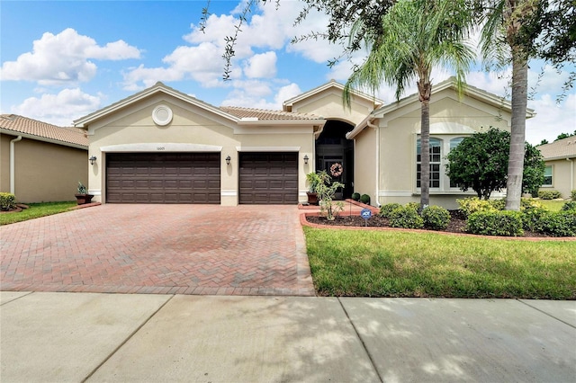 view of front facade with stucco siding, a tiled roof, decorative driveway, a front lawn, and a garage