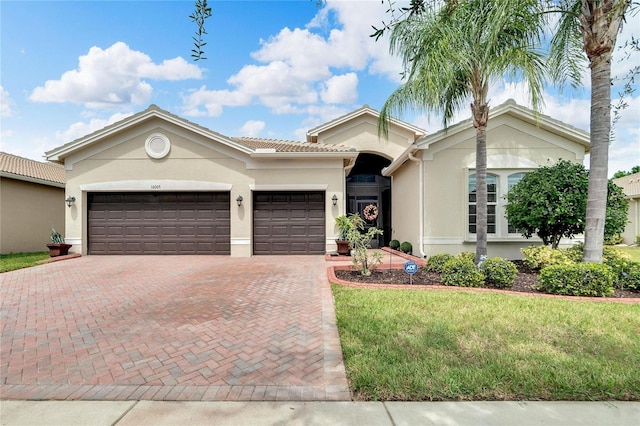 ranch-style home featuring a tile roof, stucco siding, an attached garage, a front lawn, and decorative driveway