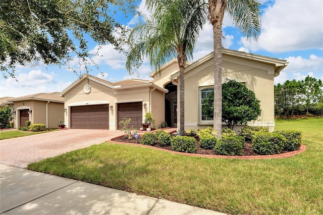 mediterranean / spanish home featuring a front yard, decorative driveway, stucco siding, and an attached garage