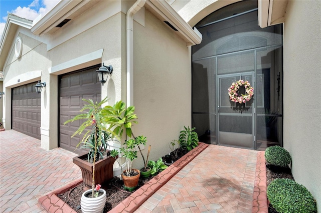 doorway to property featuring decorative driveway, stucco siding, and an attached garage