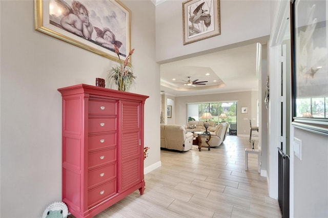 hallway with baseboards, crown molding, and a raised ceiling