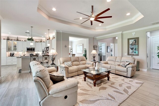 living room with light hardwood / wood-style flooring, ceiling fan, ornamental molding, and a tray ceiling