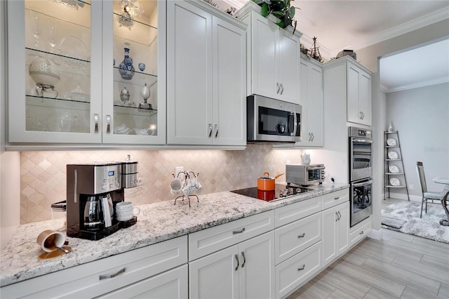 kitchen with ornamental molding, light stone countertops, stainless steel appliances, tasteful backsplash, and glass insert cabinets