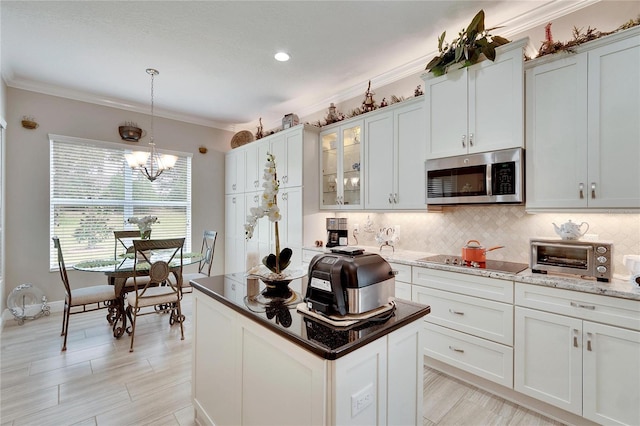 kitchen with a notable chandelier, crown molding, backsplash, black electric cooktop, and stainless steel microwave