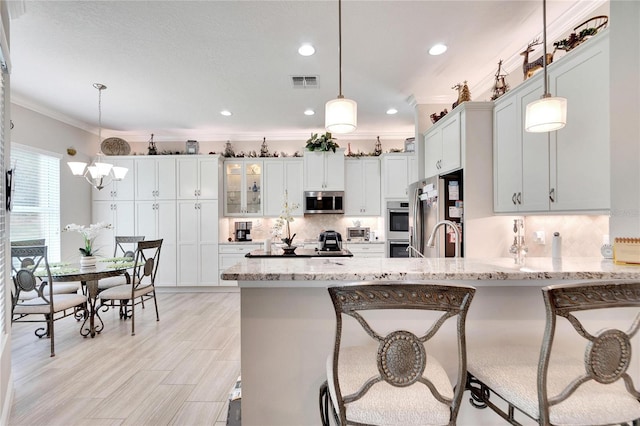 kitchen with white cabinetry, light hardwood / wood-style flooring, stainless steel appliances, light stone counters, and hanging light fixtures