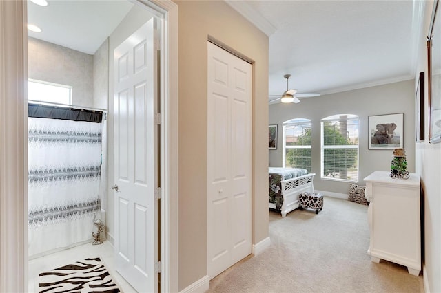 hall featuring baseboards, crown molding, and light carpet