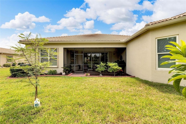 rear view of house featuring a tile roof, stucco siding, a sunroom, and a yard