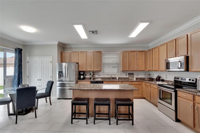 kitchen featuring dark stone counters, a breakfast bar area, a kitchen island, appliances with stainless steel finishes, and crown molding