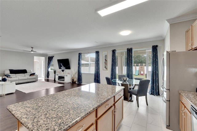 kitchen with a kitchen island, appliances with stainless steel finishes, ornamental molding, ceiling fan, and light stone countertops