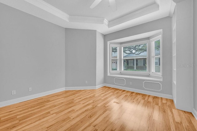 spare room with ceiling fan, light wood-type flooring, crown molding, and a tray ceiling