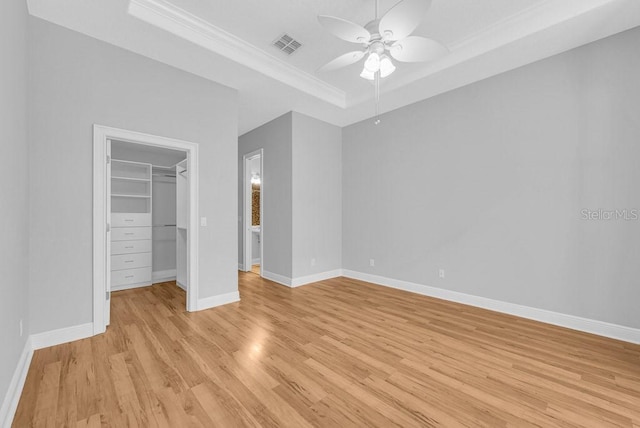 unfurnished bedroom with light wood-type flooring, a closet, a raised ceiling, a spacious closet, and ceiling fan