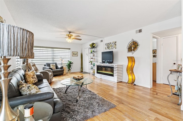 living room with ceiling fan, a textured ceiling, and light hardwood / wood-style flooring