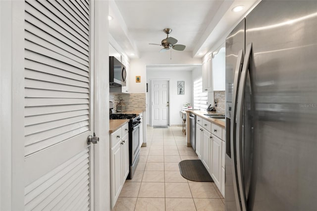 kitchen with appliances with stainless steel finishes, decorative backsplash, white cabinetry, light tile patterned floors, and ceiling fan