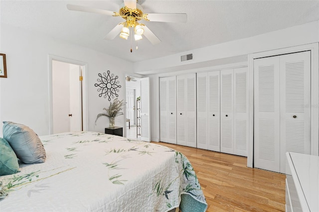 bedroom with light hardwood / wood-style flooring, two closets, ceiling fan, and a textured ceiling