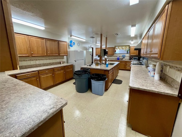 kitchen featuring a center island, tasteful backsplash, sink, white fridge, and exhaust hood