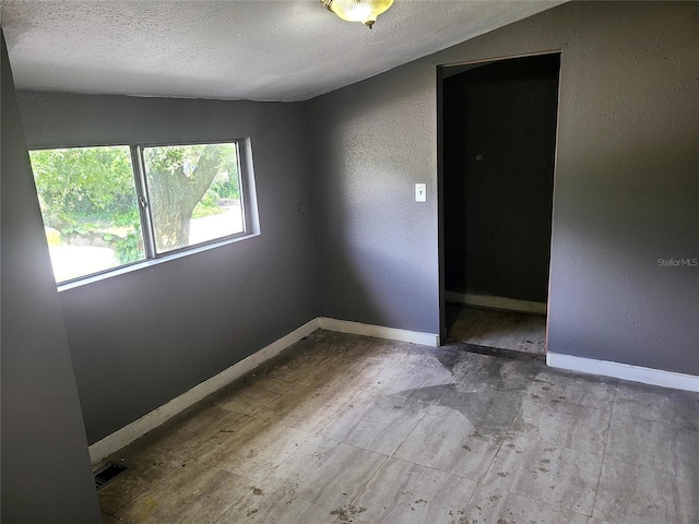 empty room with a textured ceiling and lofted ceiling