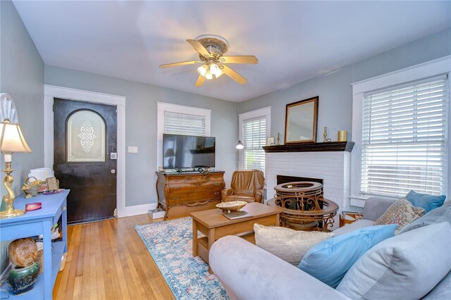 living room featuring light hardwood / wood-style flooring, a brick fireplace, and ceiling fan