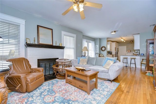 living room featuring wood-type flooring, a brick fireplace, and ceiling fan