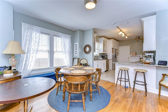 dining space with ceiling fan, sink, track lighting, and light hardwood / wood-style floors