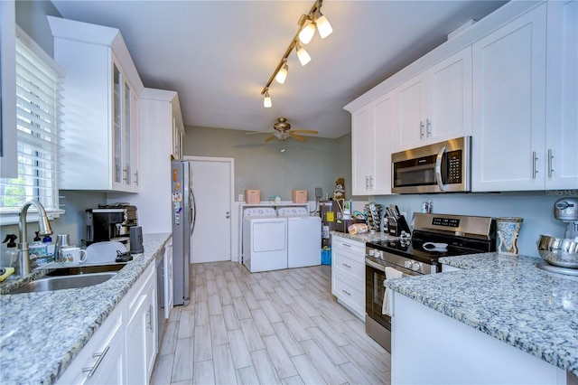 kitchen with washing machine and clothes dryer, stainless steel appliances, sink, ceiling fan, and white cabinets