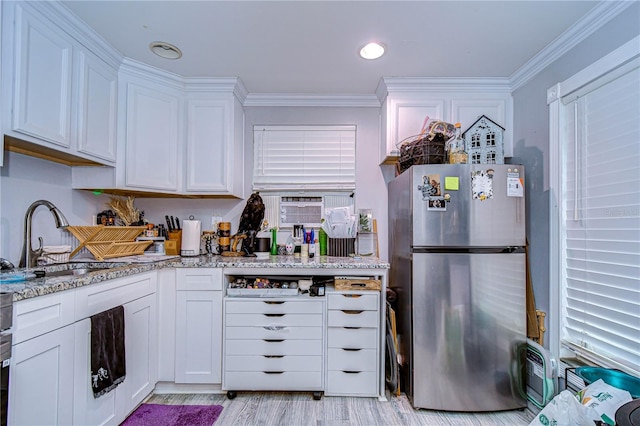 kitchen with light stone countertops, white cabinetry, stainless steel refrigerator, and ornamental molding