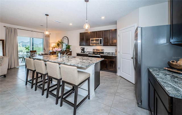 kitchen featuring pendant lighting, a breakfast bar area, an island with sink, appliances with stainless steel finishes, and light stone countertops