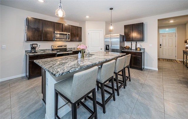 kitchen with appliances with stainless steel finishes, a center island with sink, dark brown cabinets, and decorative light fixtures