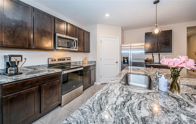 kitchen with dark brown cabinetry, light tile patterned flooring, sink, appliances with stainless steel finishes, and light stone countertops