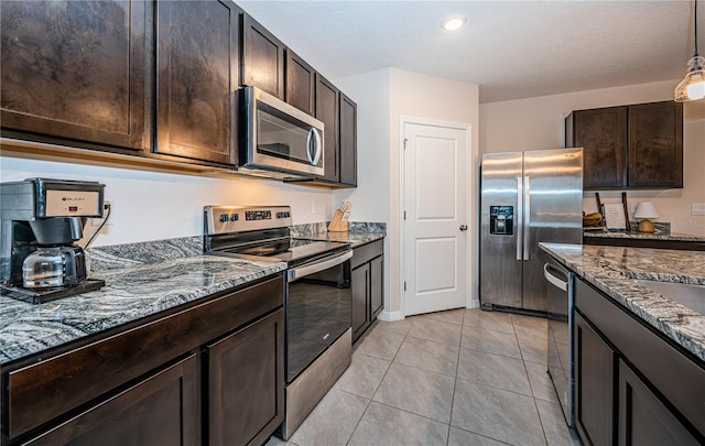 kitchen with dark brown cabinetry, hanging light fixtures, light tile patterned floors, appliances with stainless steel finishes, and dark stone counters