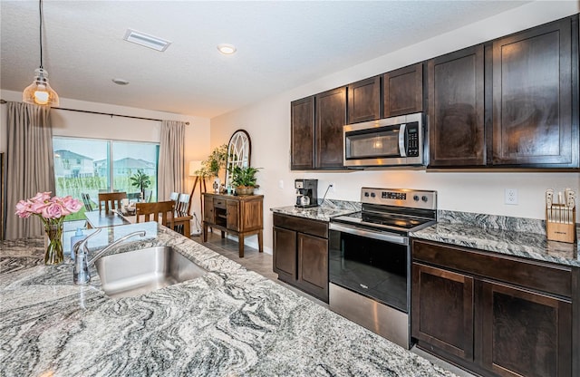 kitchen featuring light stone counters, a textured ceiling, sink, appliances with stainless steel finishes, and dark brown cabinetry